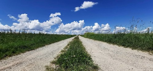 A long dirt road leads through a vast green landscape under blue skies, Franconian Forest nature