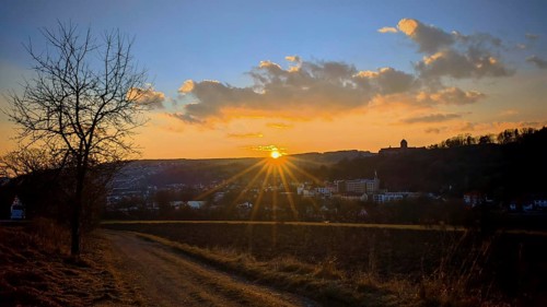 An idyllic sunset over an urban landscape with a path that leads through fields, a view towards