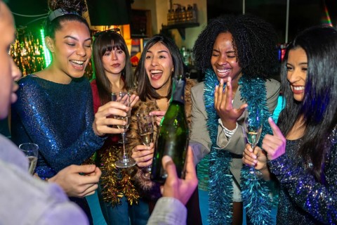 Group of excited diverse young adult friends smiling and laughing while celebrating a special