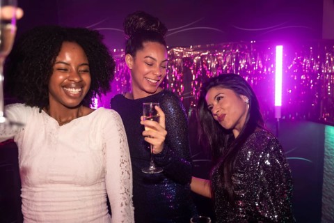 Three diverse women friends enjoying a night out, toasting with champagne and smiling while