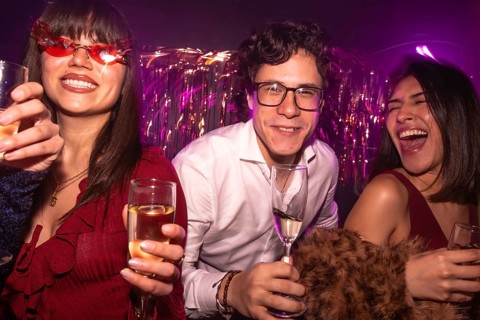 Young friends enjoying a vibrant night out with drinks, smiling and laughing under club lights,