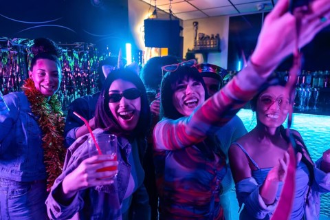 Young diverse friends enjoying a lively nightclub party, smiling, dancing, and posing for a selfie,