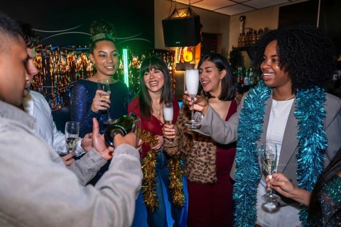 Diverse friends celebrating indoors with festive decorations as one man pours champagne into