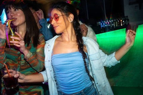 Young women enjoying nightlife, dancing and drinking cocktails with neon light reflections at a