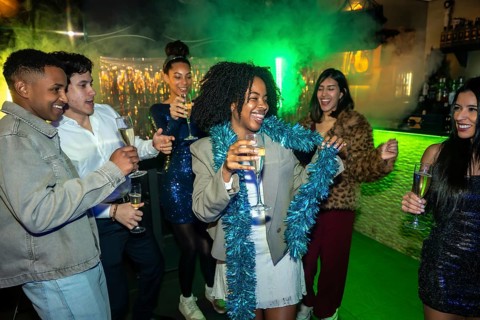 Group of diverse young adults having fun, dancing, and laughing while holding champagne flutes at a