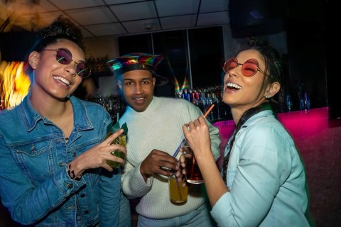 Diverse group of young people socializing at a bar, laughing and holding cocktails under colorful