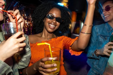Young happy diverse women enjoying a night out, smiling and dancing together with drinks in a