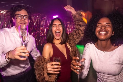 Happy diverse friends clinking champagne in a vibrant nightclub, dancing under dynamic lights and