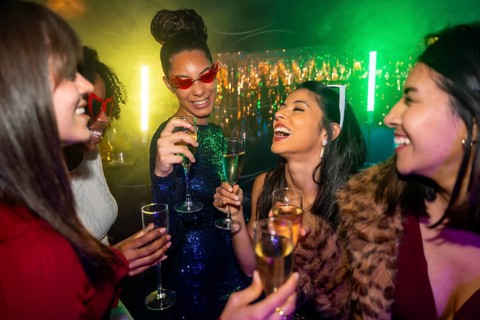 Joyful multiracial women laughing and clinking champagne glasses at a vibrant nightclub party,