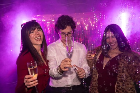 Friends cheering and having fun while celebrating a party with champagne and bubbles, experiencing