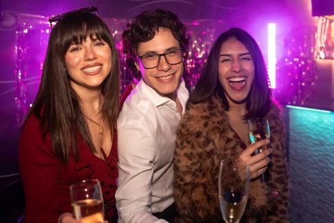 Three diverse young friends celebrating and having fun together at a vibrant nightclub, holding