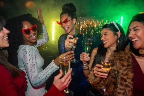 Diverse group of smiling young women toasting with champagne in a vibrant nightclub, celebrating a