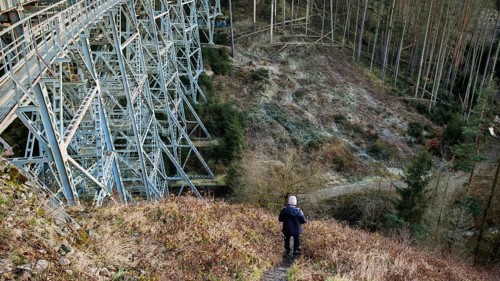 Hikers on a path next to a large metal-textured bridge, old railroad bridge in the forest,