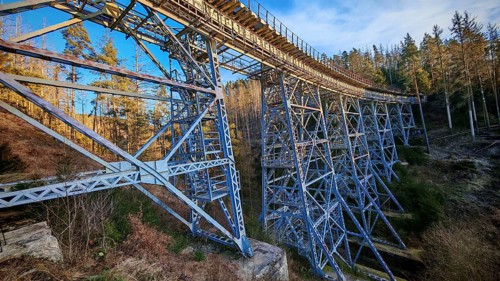 Side view of an extended metal bridge, old railroad bridge leading through a forest,