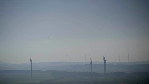 Blurred range of hills with isolated wind turbines in morning fog under blue sky, Franconian Forest
