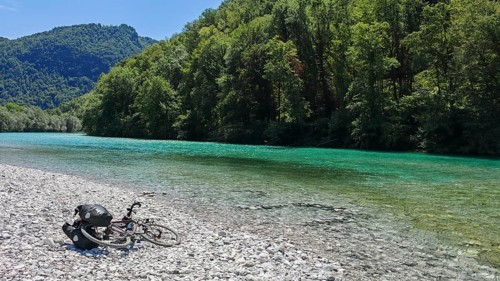 Bicycle lying next to a clear river on a pebble beach surrounded by forest, Soca Valley, Slovenia