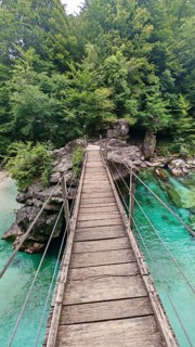 Wooden suspension bridge over green-turquoise water, surrounded by thick forest, Soca Valley,