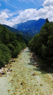 A clear river flows through a wooded mountain landscape under a blue sky, Soca Valley, Slovenia