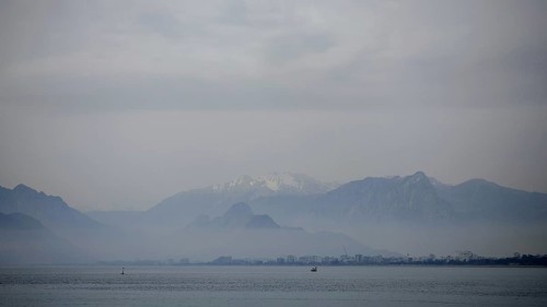 Blurred mountains and a distant city in fog over a calm sea with boats, Antalya, Turkey