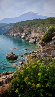 Rocky coast with turquoise water and a snow-capped mountain Tahtali Dagi in the background,