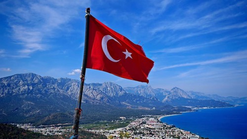 Turkish flag flies over a coastal town with mountains and blue sky, Kemer, Turkey