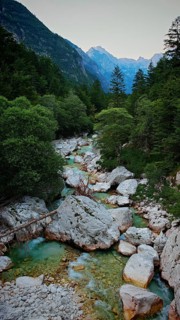 A clear mountain river surrounded by rocks and trees with mountains in the background, Soca Valley,