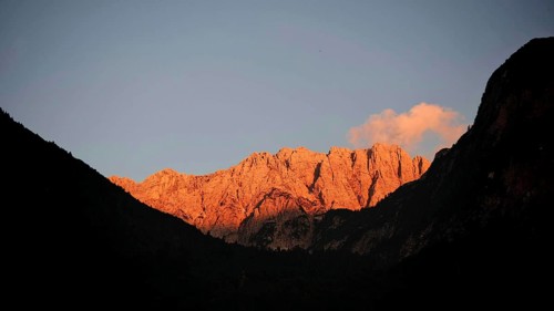 Mountains at sunset with golden rocks, alpine glow, and dark silhouettes in the foreground,