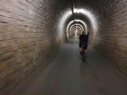 A cyclist crosses a long, illuminated stone tunnel, Slovenia