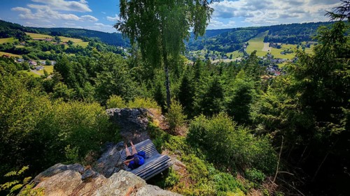 A panorama from a viewpoint with a person on a bench with a view of a picturesque valley,