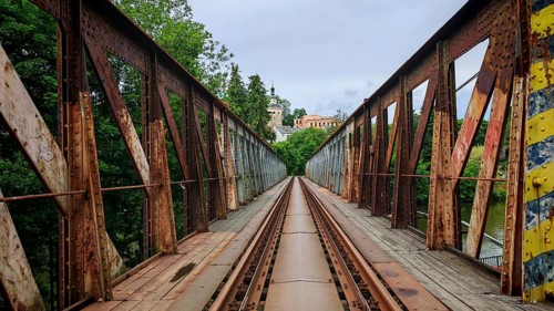 Old, rusty metal railroad bridge leads through green forests to a remote small town, Loket, Czech