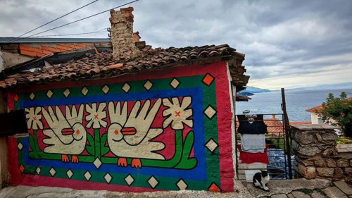 Colourfully painted house façade with dove motifs, laundry hanging to dry with cat in the