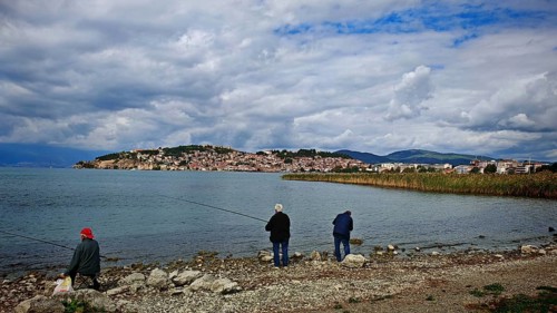 Fishermen on the shore of a lake with a view of a city in the background under cloudy sky, Ohrid,