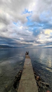 A long jetty leads into the calm sea under a cloudy sky that creates a peaceful atmosphere, Lake