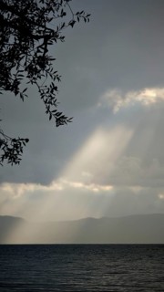 Dramatic ray of light falling through clouds onto a calm lake, Lake Ohrid, North Macedonia