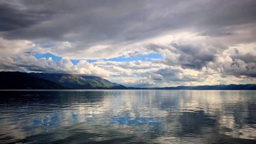 Extensive lake with reflective, dramatic clouds and calm water and mountains in the background,