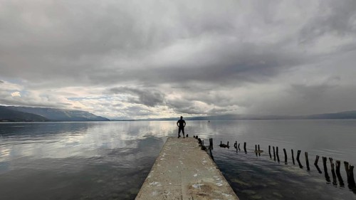 A man stands alone on a jetty that juts into a cloud-covered lake, Lake Ohrid, North Macedonia