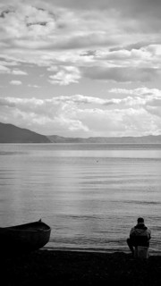 An angler is quietly looking at the shore of a lake, accompanied by a boat in black and white, Lake