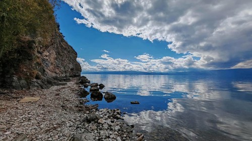 A peaceful rocky coast with a lake whose water reflects the clouds of the dramatic sky, Lake Ohrid,