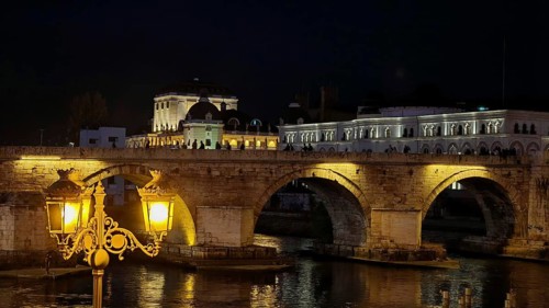 Illuminated bridge at night over a river with historic architecture, Skopje, North Macedonia