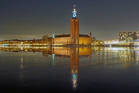 Night scene of a town hall with illuminated tower, peaceful reflection on calm water, Nobel Prize,