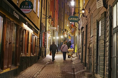 Narrow alley at night with old buildings and warm light. People walking on cobblestones, Gamla