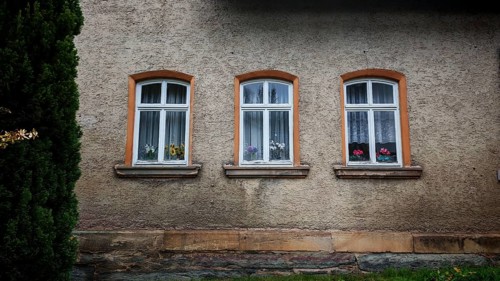 Three glazed windows with curtains and flowers, orchids (Orchidaceae) on a rustic house façade,