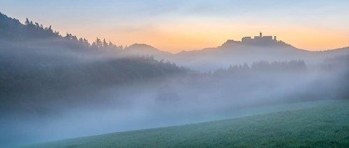 View of Wartburg Castle in the Thuringian Forest at sunrise, morning fog and dawn, meadow with dew,