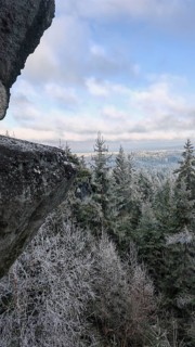 A large rock above a snowy landscape surrounded by fir trees with a cloudy sky in the background,