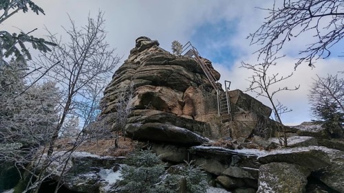 An impressive rock with a metal staircase, ladder, next to it, surrounded by snow-covered trees