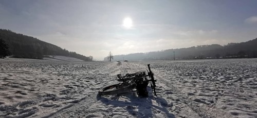 Cycling in the snow on a wide area with rolling hills in the background under the sun, Frankenwald