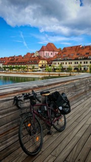 Bicycle on a bridge across a river with historic buildings in the background under cloudy sky,