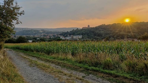 A trail leads along fields with a village in the background at sunset, Kronach with a view of