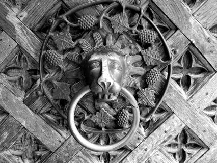 An ornate metal door knocker in the shape of a lion's head against a wooden background, Poland