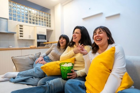 Three young adult female friends enjoying a relaxing movie night at home, laughing together,